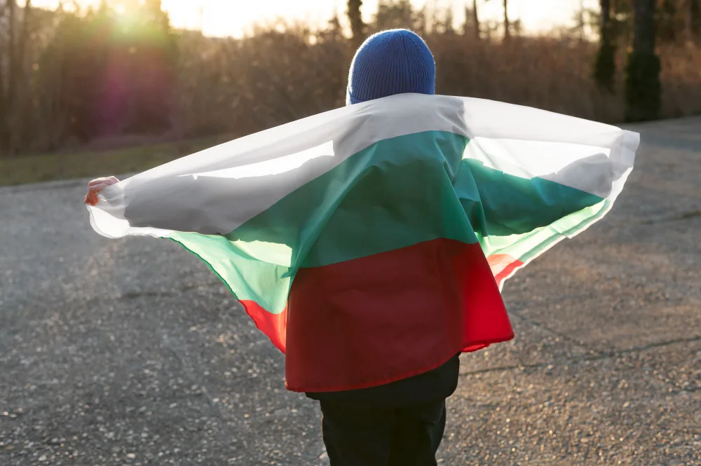 Ребенок держит за спиной флаг Болгарии и смотрит на закат