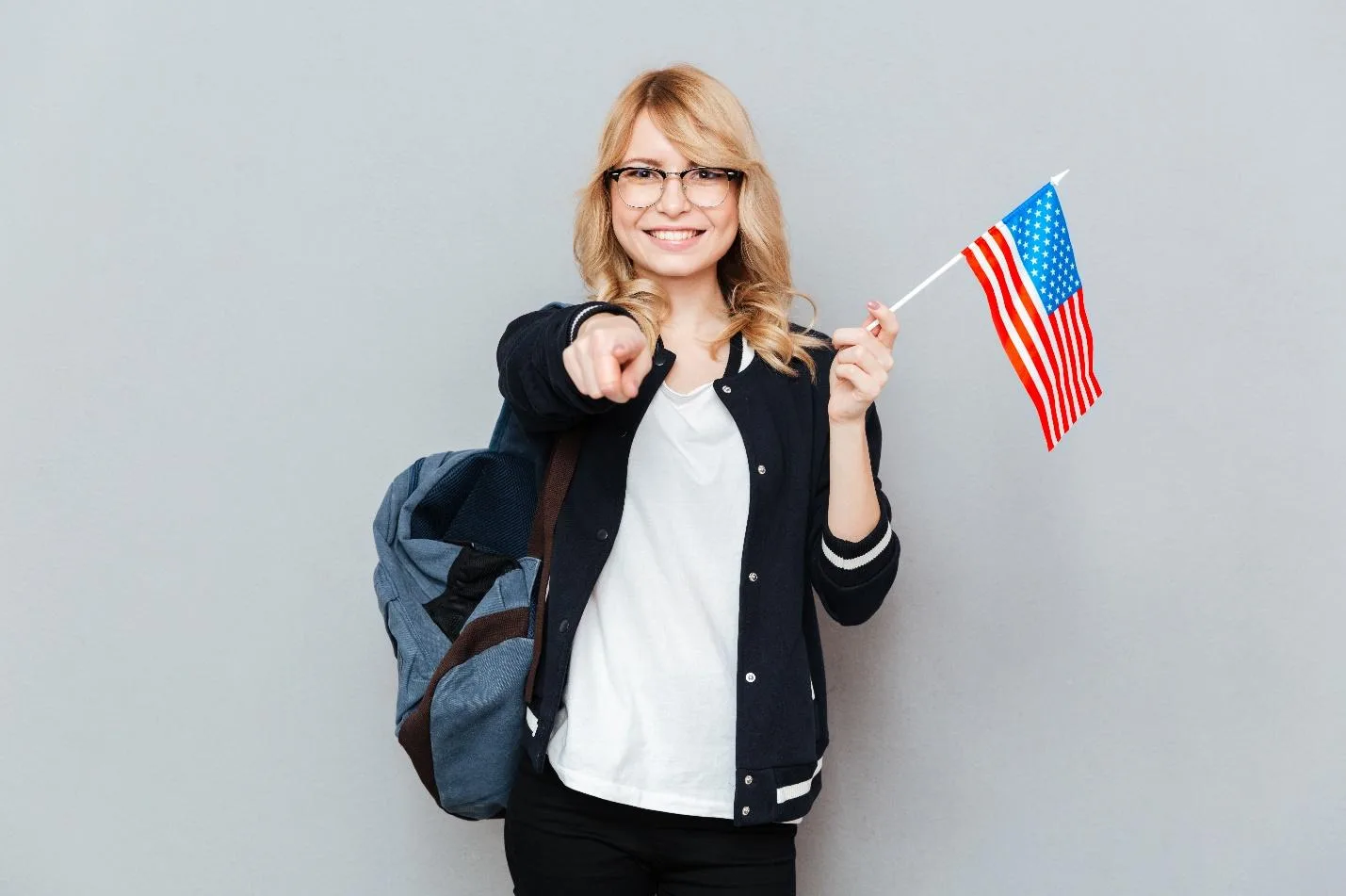 Девушка с рюкзаком и флагом США показывает пальцем