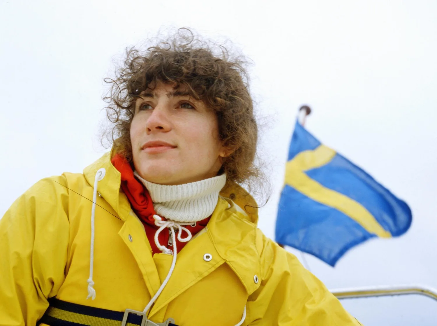 Кудрявая девушка в жёлтой куртке около флага Швеции