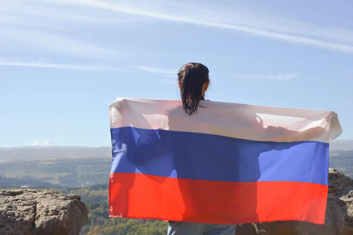 Девушка держит флаг России на спине и смотрит на пейзаж